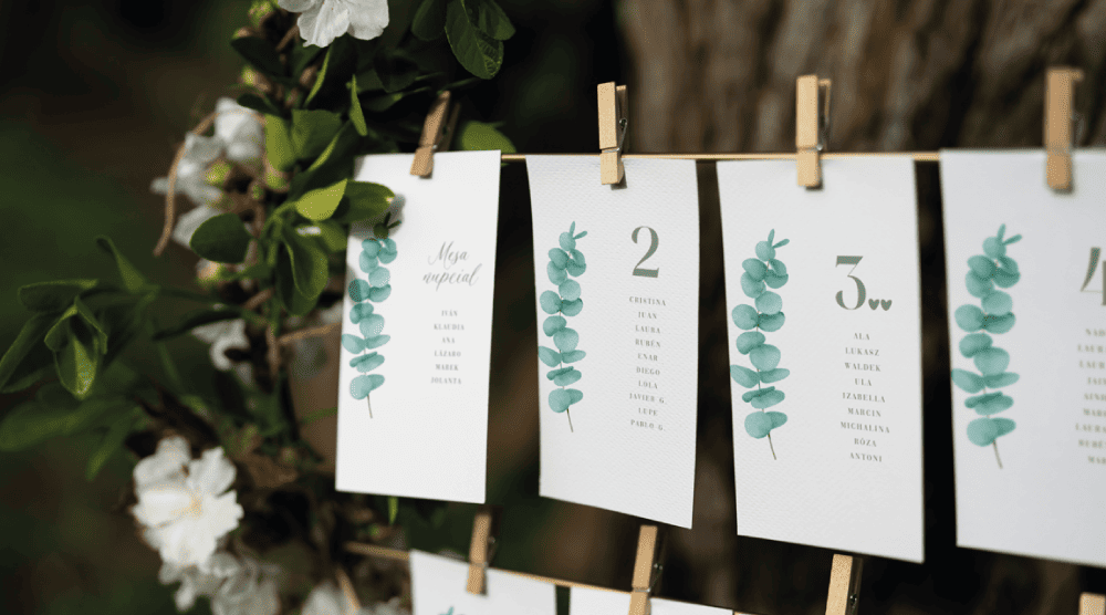 Sitting plan de boda con tarjetas colgadas y diseño botánico, numeración de mesas personalizada y estilo gráfico natural.