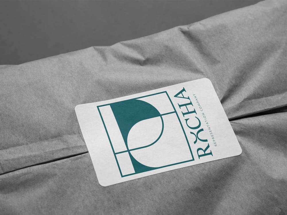 Etiqueta con el logotipo de Rocha sobre tejido gris, ejemplo de aplicación de identidad visual y branding elegante desarrollado por Landa Estudio para la marca.