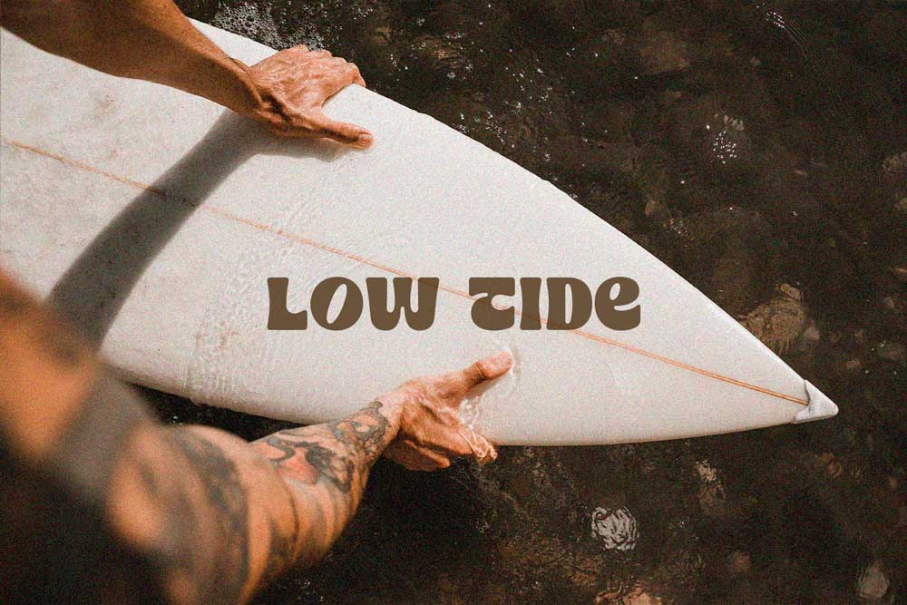 Logotipo Low Tide aplicado sobre una tabla de surf, diseño gráfico inspirado en el movimiento del mar y la cultura surfista.