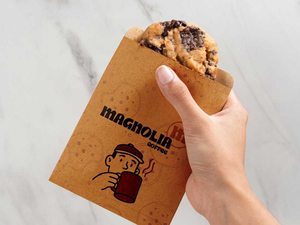 Mano sosteniendo una galleta en envoltorio de papel ilustrado, ejemplo de diseño gráfico aplicado a packaging artesanal.
