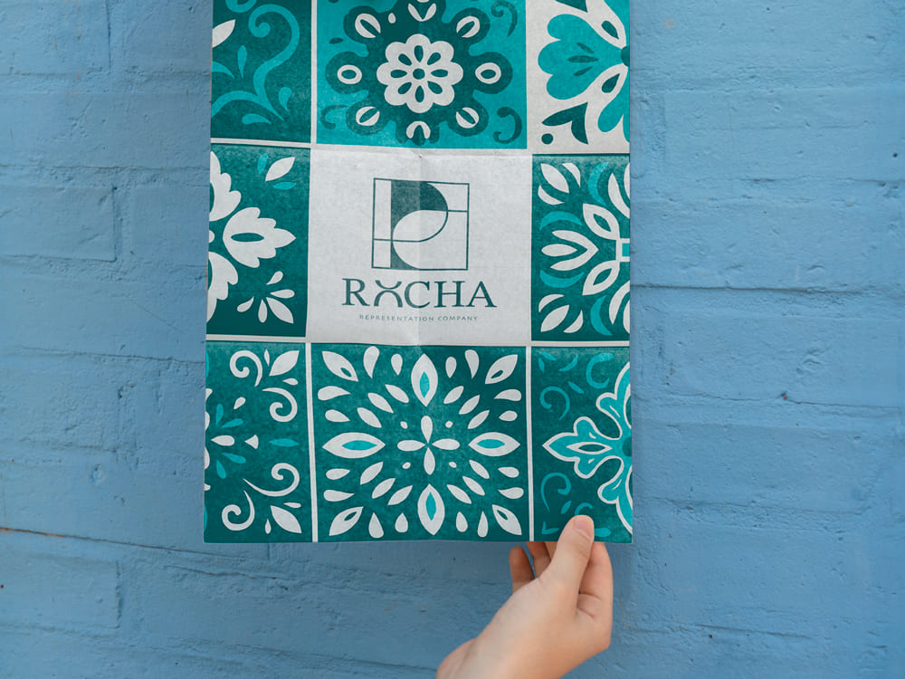 Composición con una mano colocando un azulejo con el logotipo de Rocha, representación visual del proyecto de branding, identidad corporativa y diseño de marca desarrollado por Landa Estudio.